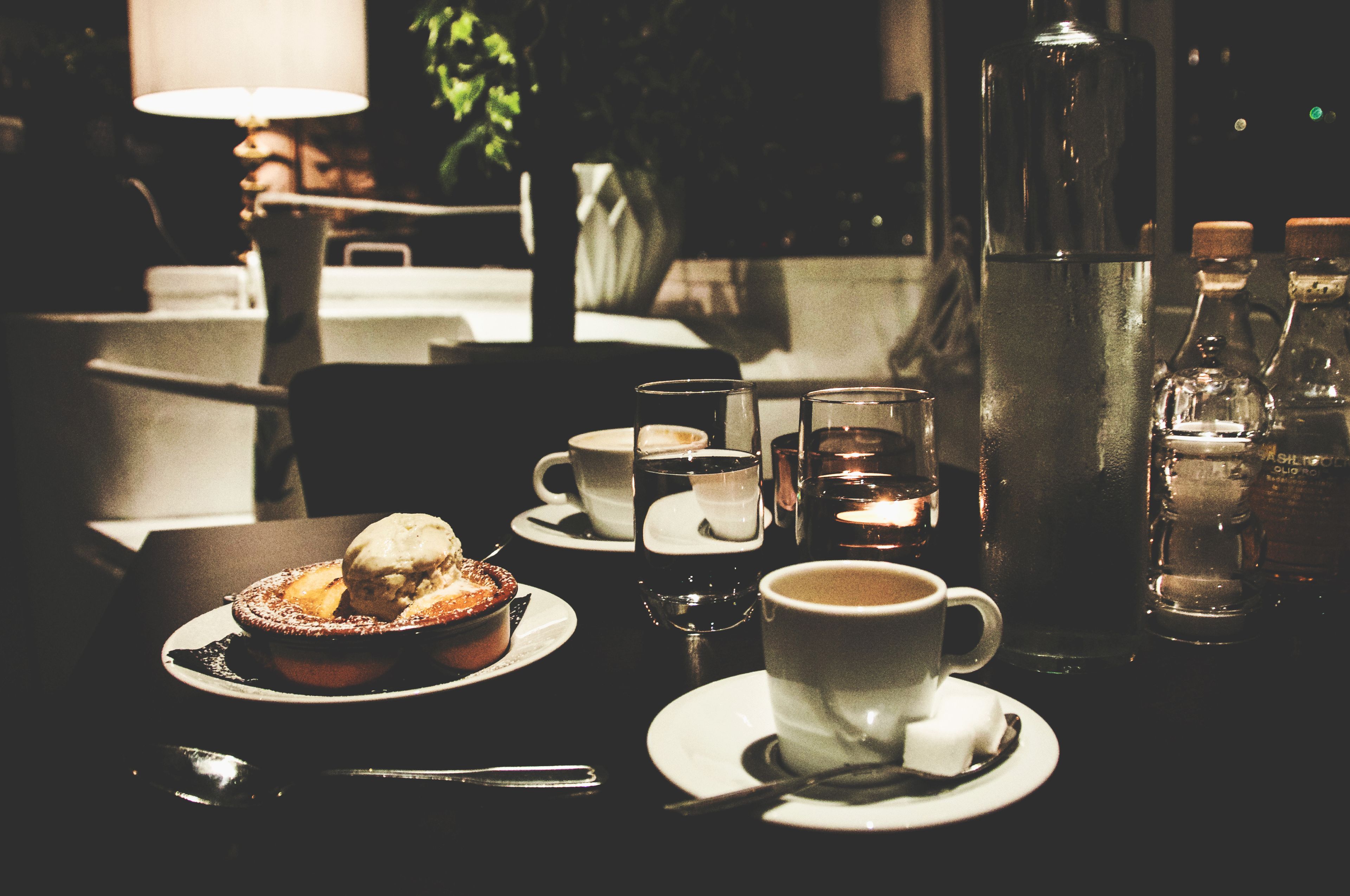 A dining table with a dessert, cups, and a candle.
