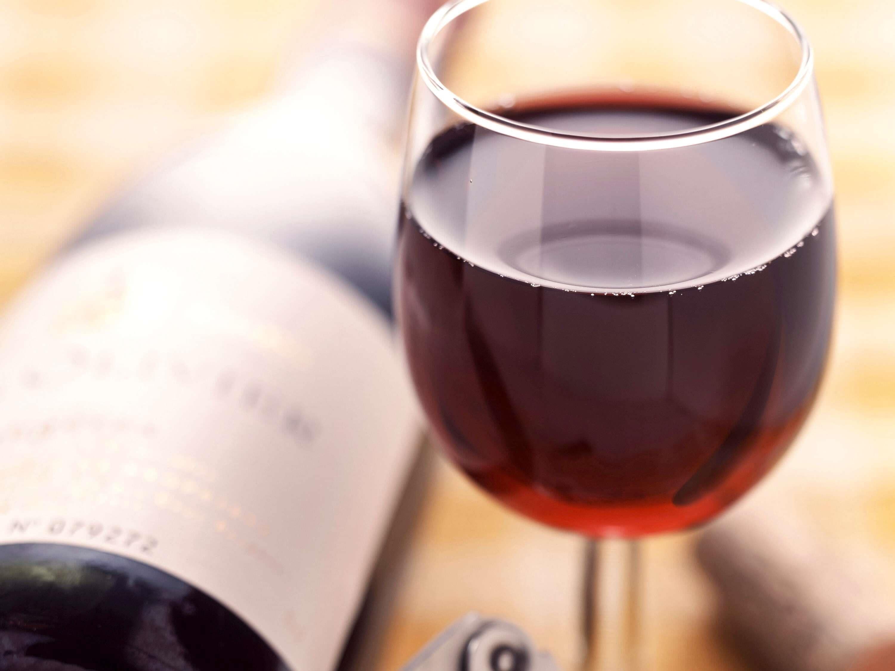 A wine glass filled with red wine next to an open wine bottle.