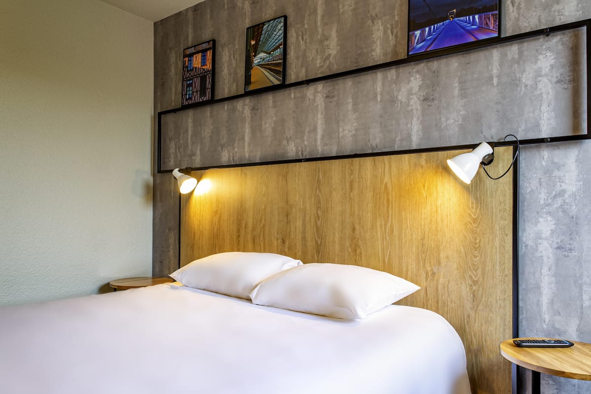 A modern hotel room with a large bed, wooden headboard, and two wall-mounted reading lamps.