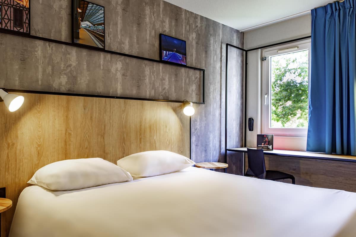 A modern hotel room with a large bed, a desk, and a window with curtains.