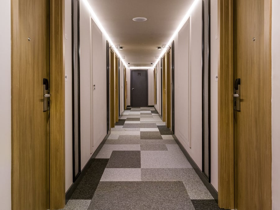 Un couloir d’hôtel avec des portes en bois, un tapis à carreaux et un éclairage au plafond.