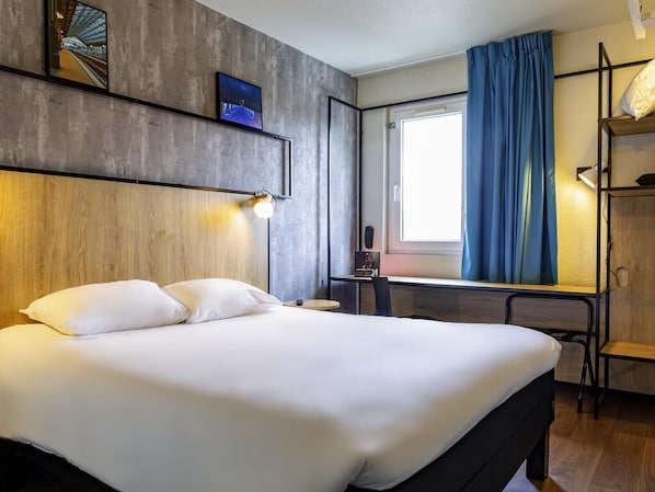 Hotelkamer met een groot bed, een bureau, een stoel, een raam met gordijnen en een tv aan de muur.