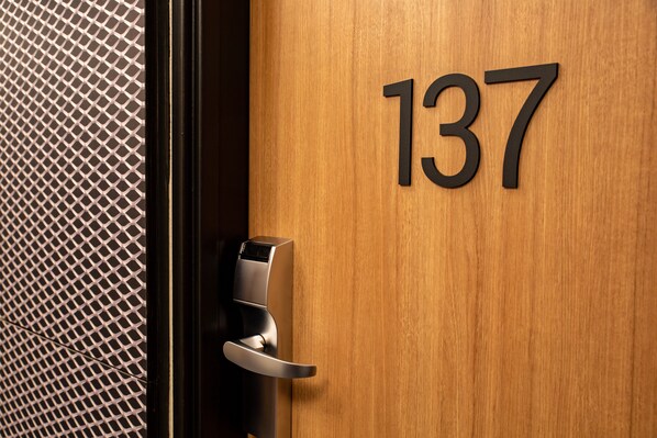 Una puerta de madera con el número 137, un picaporte moderno y un panel de malla.