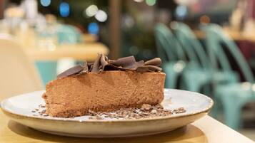 Una porción de pastel de chocolate en un plato con virutas de chocolate encima, sobre una mesa en un restaurante.