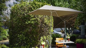 Un patio al aire libre con una mesa, sillas, un paraguas grande y una planta en maceta.