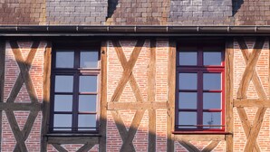 Un edificio con entramado de madera que muestra tres ventanas, cada una con marco de madera y contraventanas rojas.