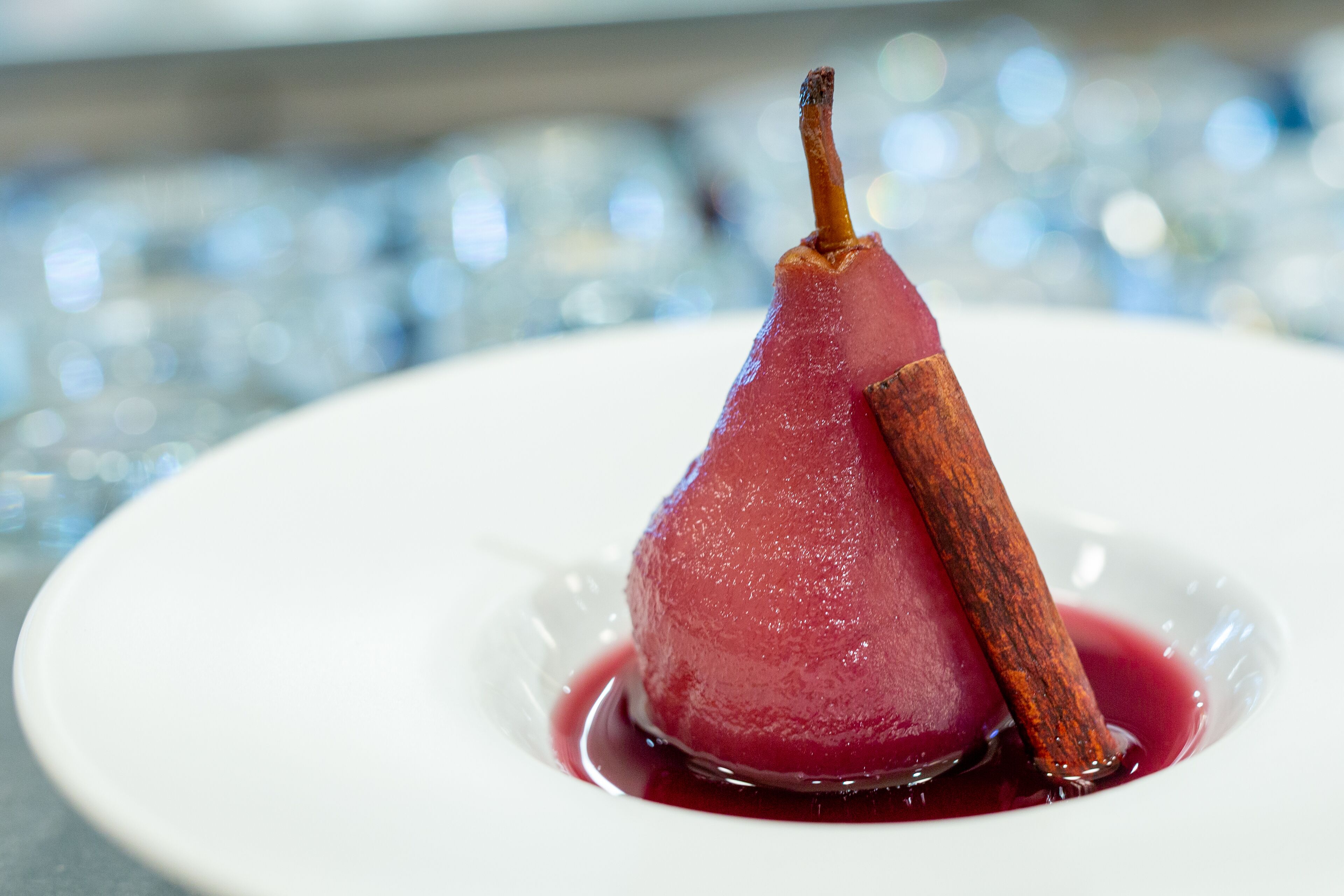 A pear dessert on a white plate with a cinnamon stick.