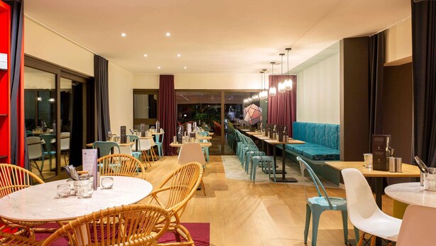 Un restaurante moderno con mesas redondas, sillas de mimbre y una barra larga con asientos azules.