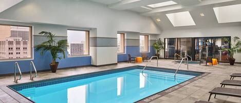 An indoor swimming pool with clear markings, a sunroof, and seating areas.