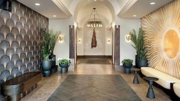 A modern lobby with a herringbone-patterned wall, a central chandelier, and a seating area with a sunburst-patterned backdrop.