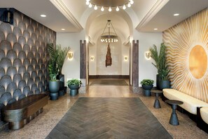 Um lobby moderno com parede em padrão herringbone, um lustre central e uma área de estar com fundo em padrão de raios de sol.