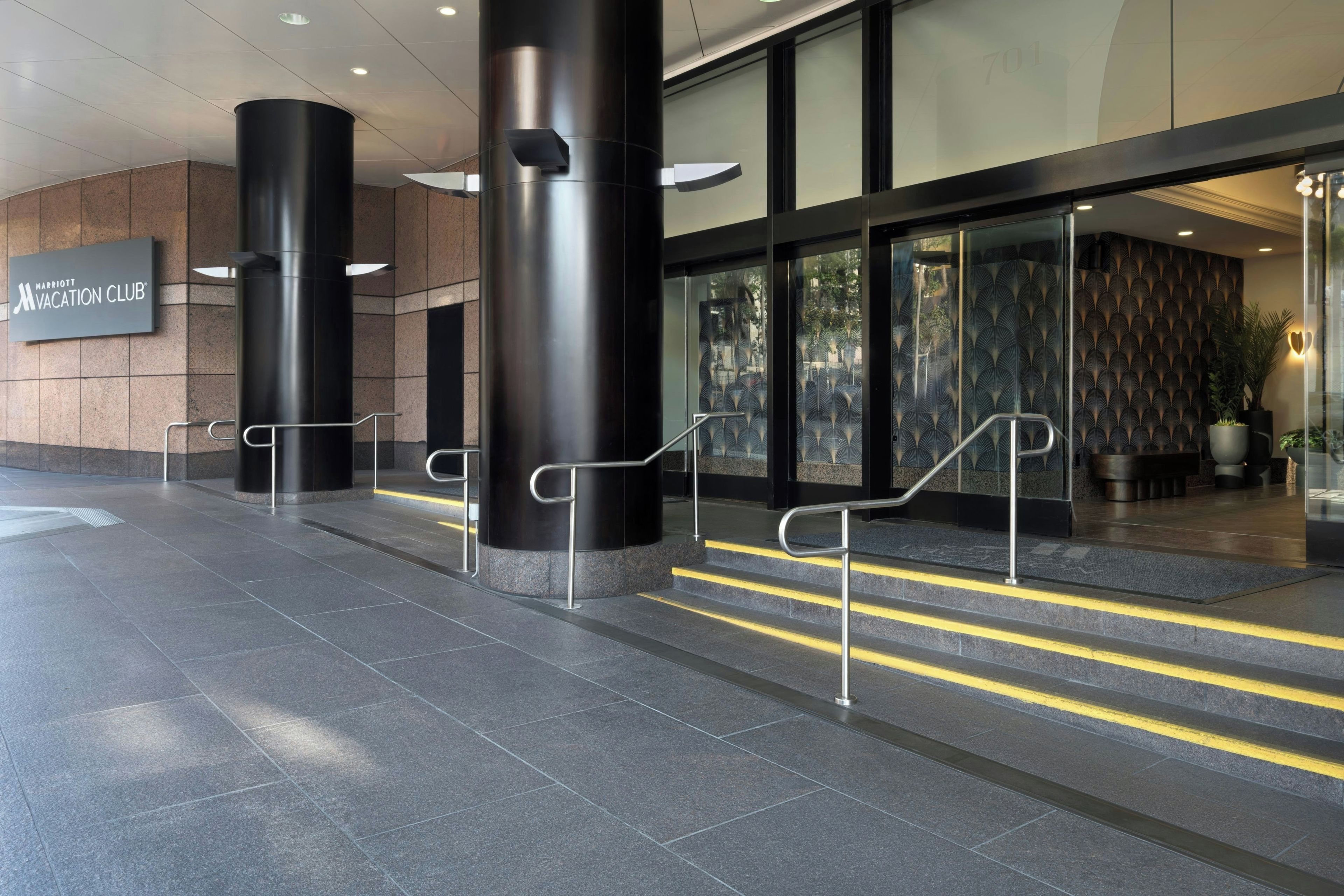 Een moderne hotelentree met een bord voor de Marriott Vacation Club, een trap die naar de lobby leidt, en een bekeken muur.