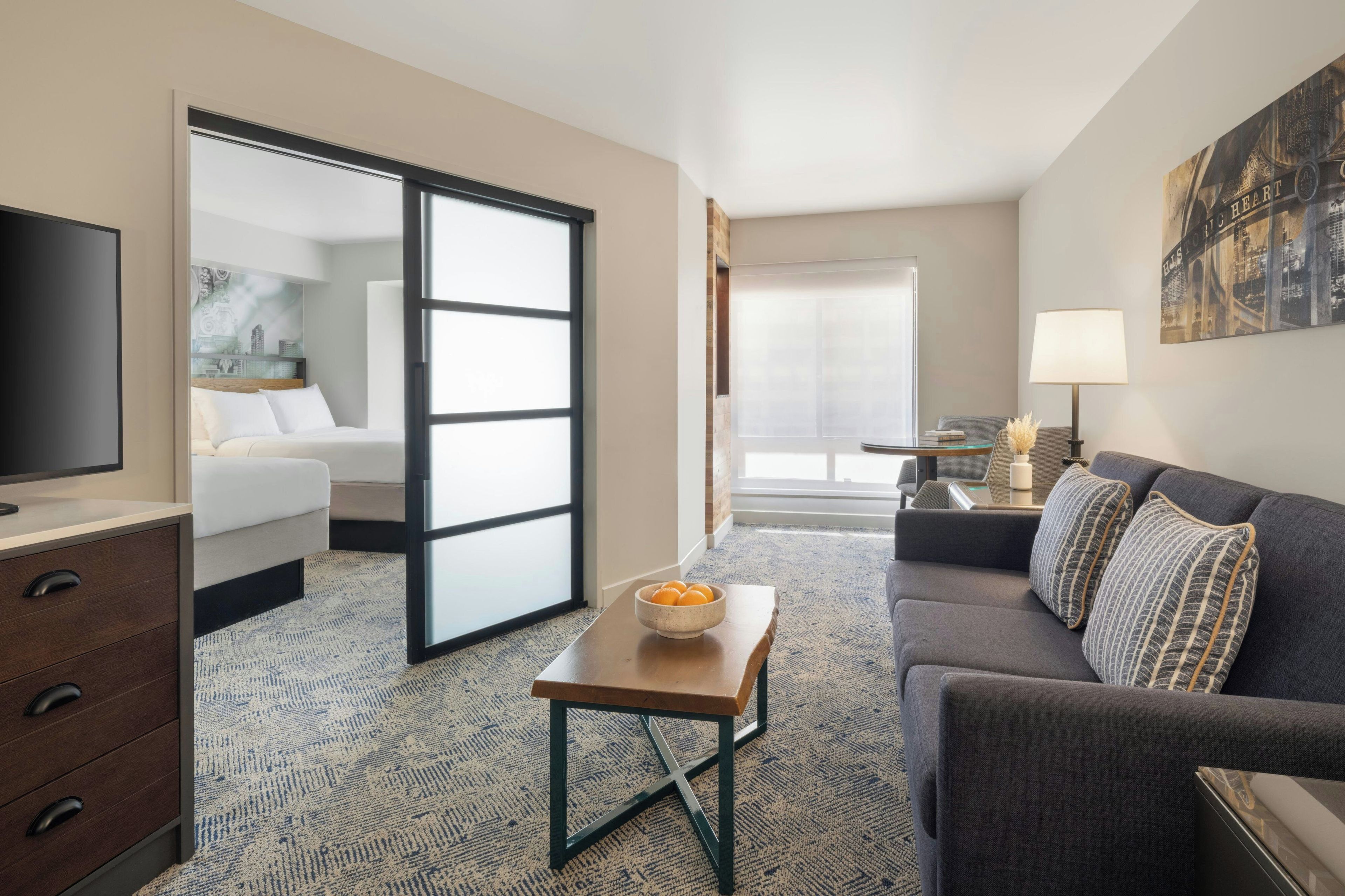 A hotel room with a bed, a sofa, a TV, a desk, and a large window.