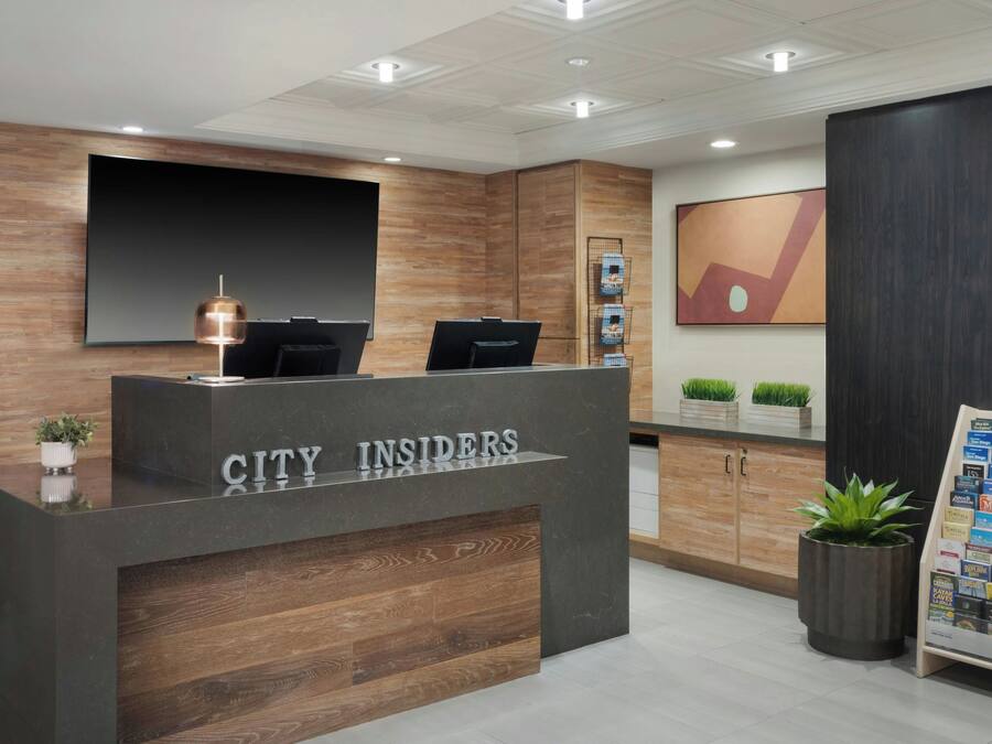 Een receptiebalie met de tekst 'CITY INSIDERS', een flatscreen televisie en een plant aan de linkerkant.