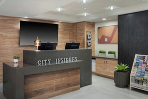 Balcão de recepção com a placa 'CITY INSIDERS', uma televisão de tela plana e uma planta à esquerda.