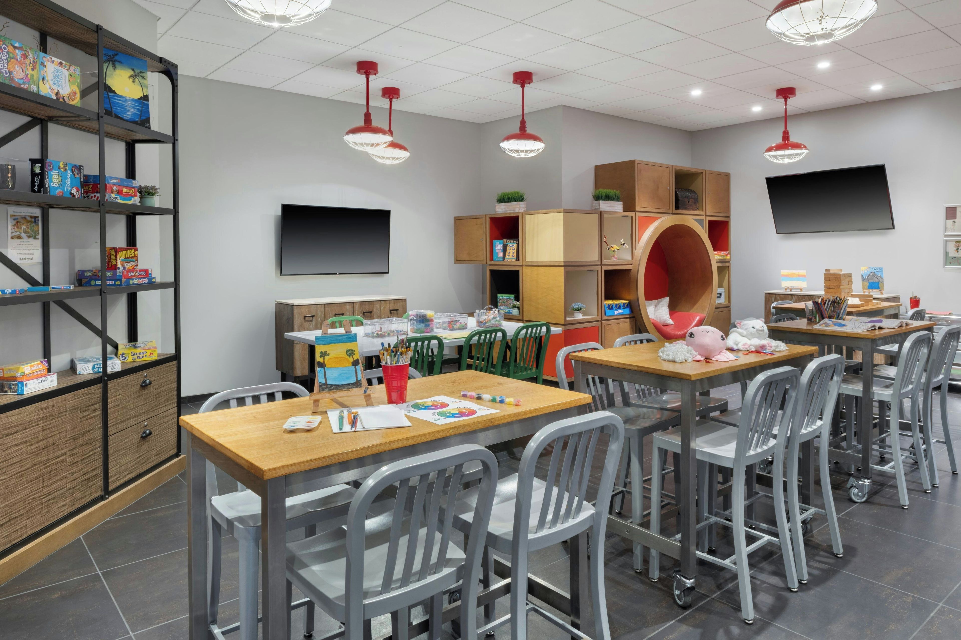 A classroom with tables, chairs, a TV, and shelves with educational materials.