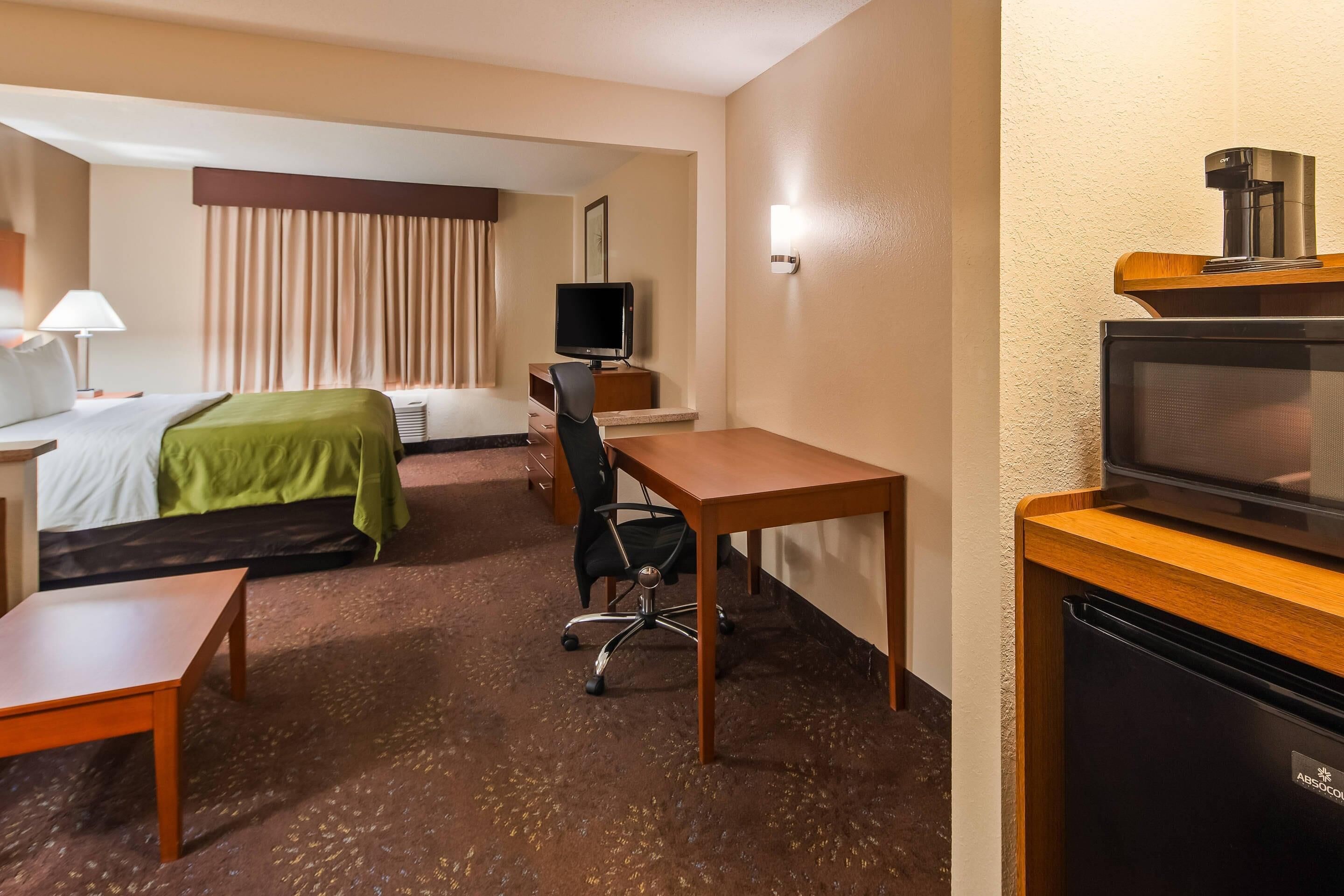 Et hotelværelse med seng, skrivebord, stol, fjernsyn og minibar.