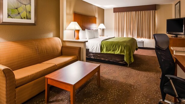 A hotel room with a sofa, a bed with a green blanket, a desk with a computer, and a TV. - Quality Inn Tomah (Tomah)