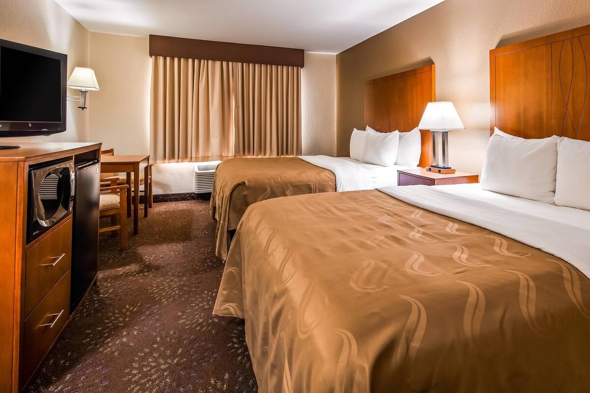 A hotel room with two beds, a TV, a desk, and a lamp.