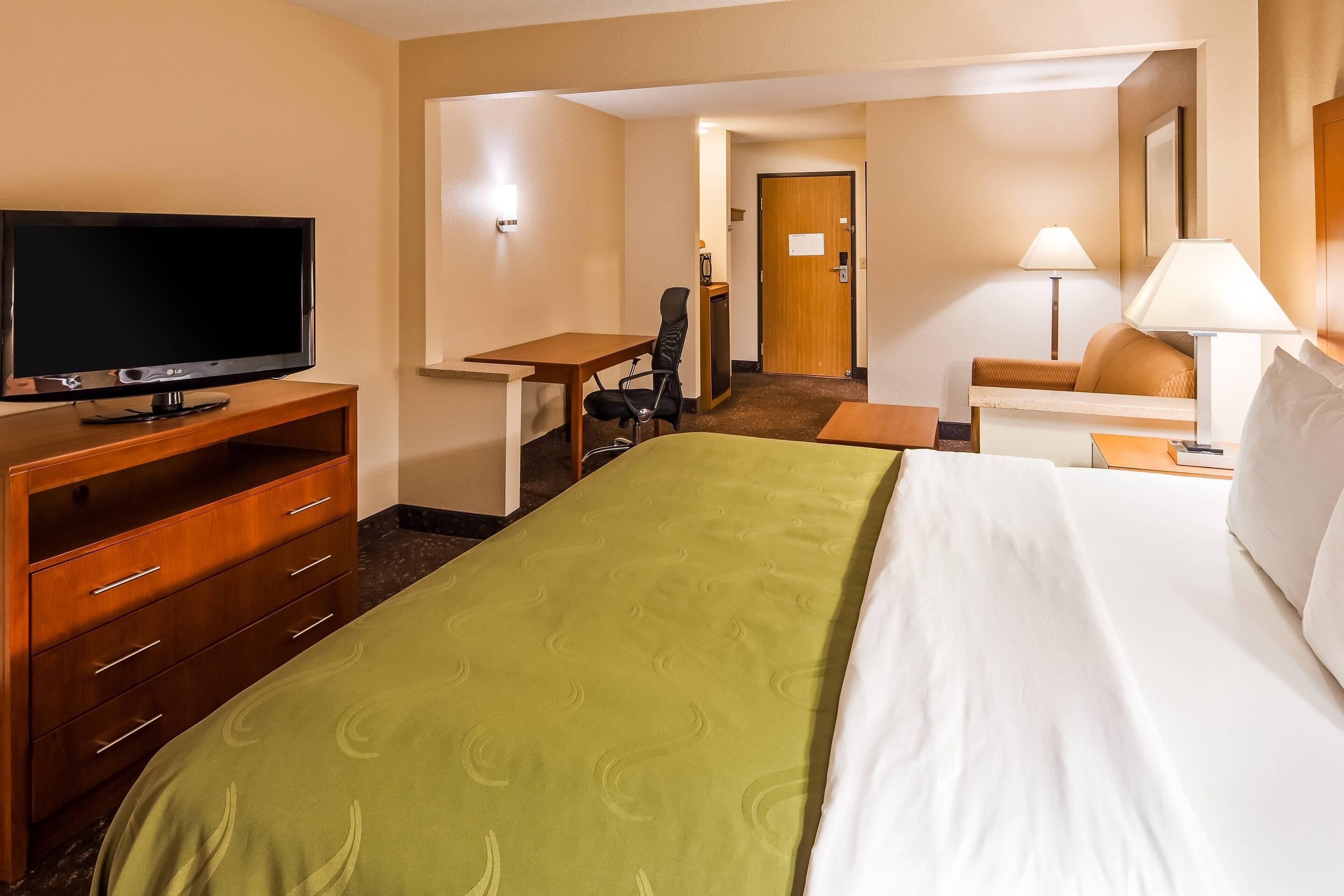 Una habitación de hotel con cama, escritorio, silla, televisor y lámpara.