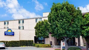A Days Inn & Suites building with a parking lot, a large tree, and a signboard. - Days Inn & Suites by Wyndham Fullerton (Fullerton)