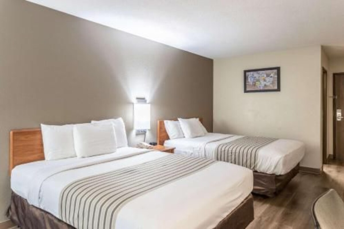 Une chambre d’hôtel avec deux lits, une table de chevet, une chaise et un tableau encadré au mur.