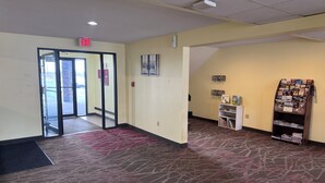 A hotel lobby with a reception desk, a bulletin board, and a glass door entrance.