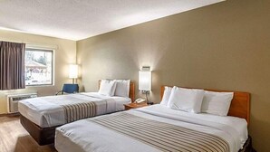 A hotel room with two beds, a desk, a chair, a lamp, and a window with curtains.