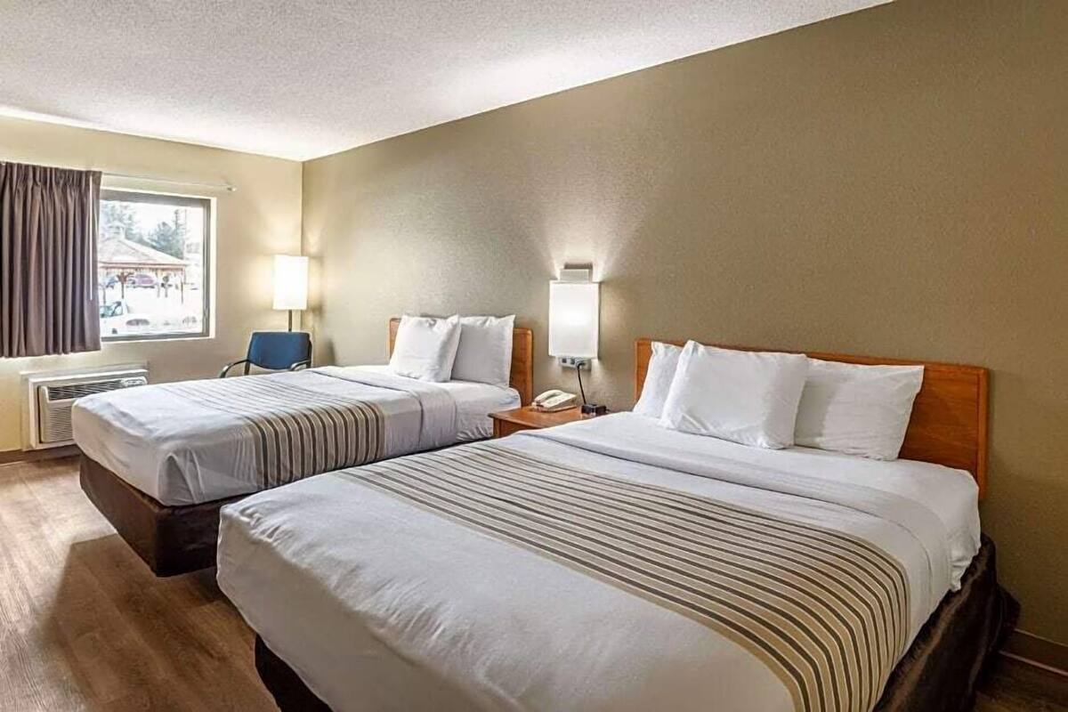 A hotel room with two beds, a desk, a chair, a lamp, and a window with curtains.
