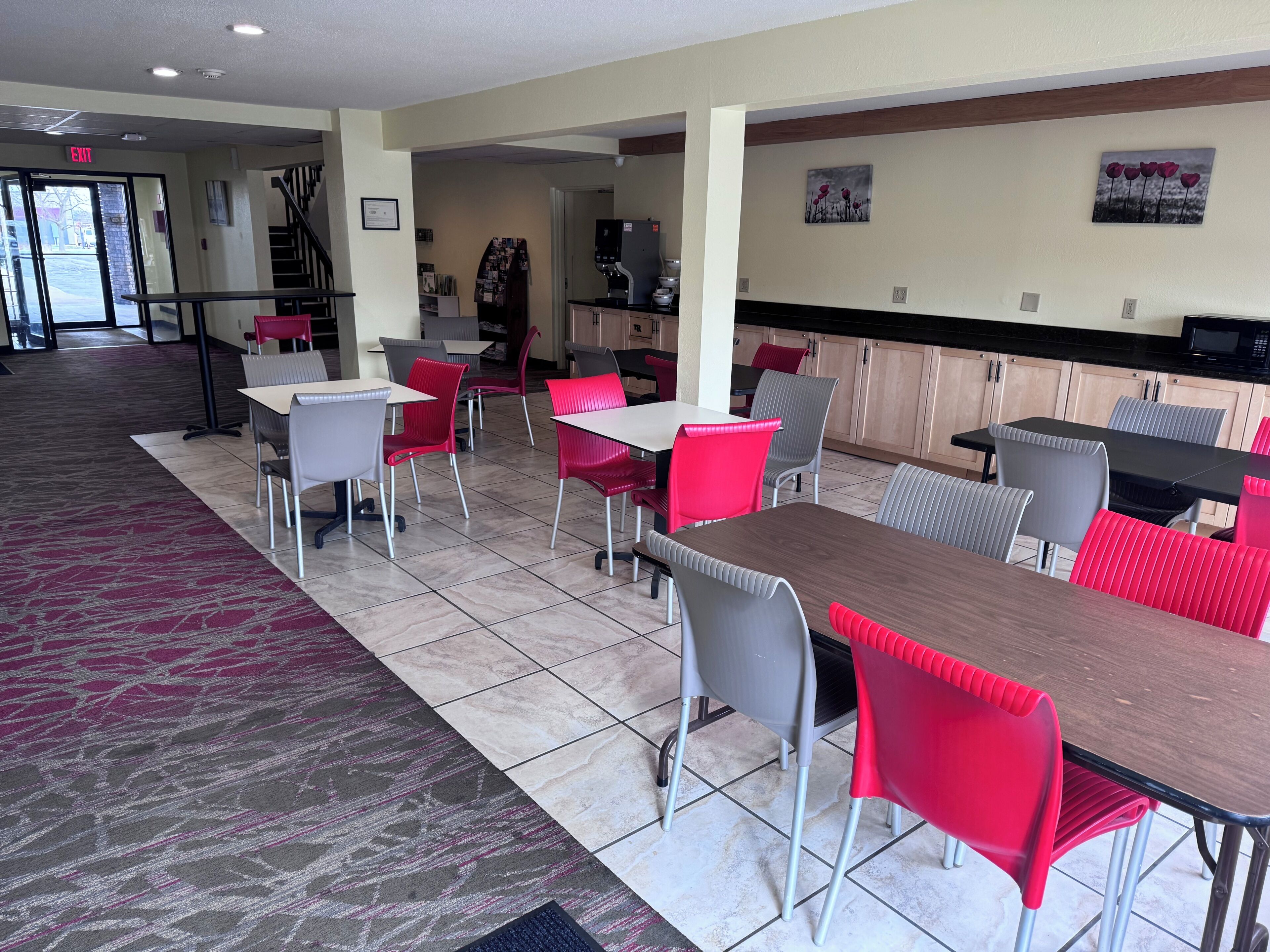 Een restaurantgedeelte van een hotel met meerdere tafels en stoelen, een keuken op de achtergrond en een nooduitgang.