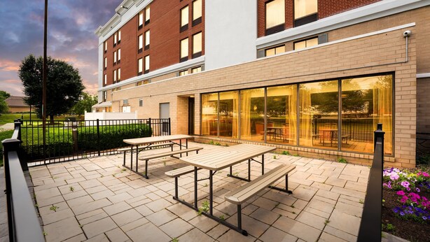 A courtyard with picnic tables, a brick building, and a glass door entrance. - Comfort Inn Lehigh Valley West - Allentown (Allentown)