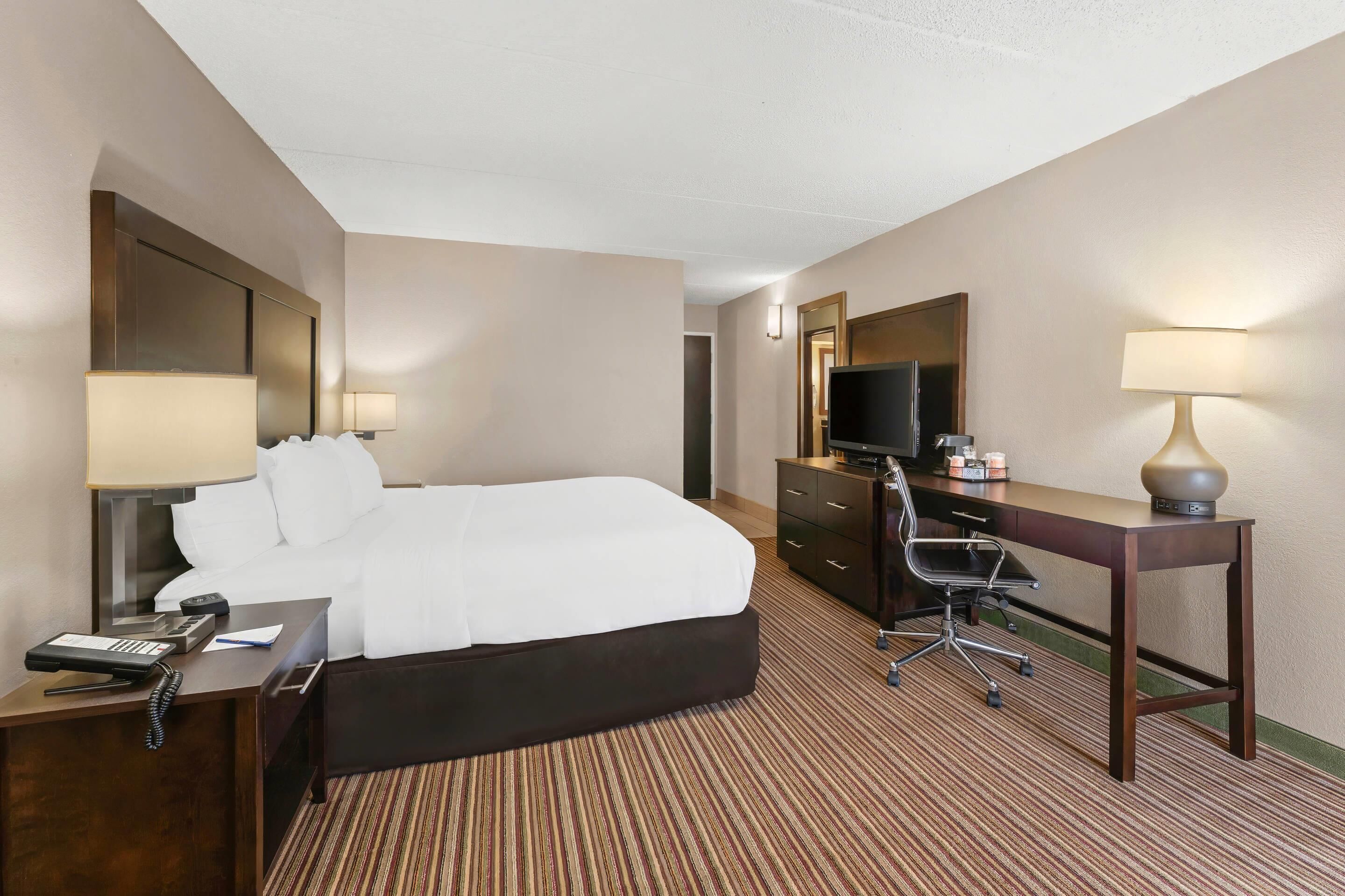 A hotel room with a large bed, a desk with a chair, a television, and a lamp.