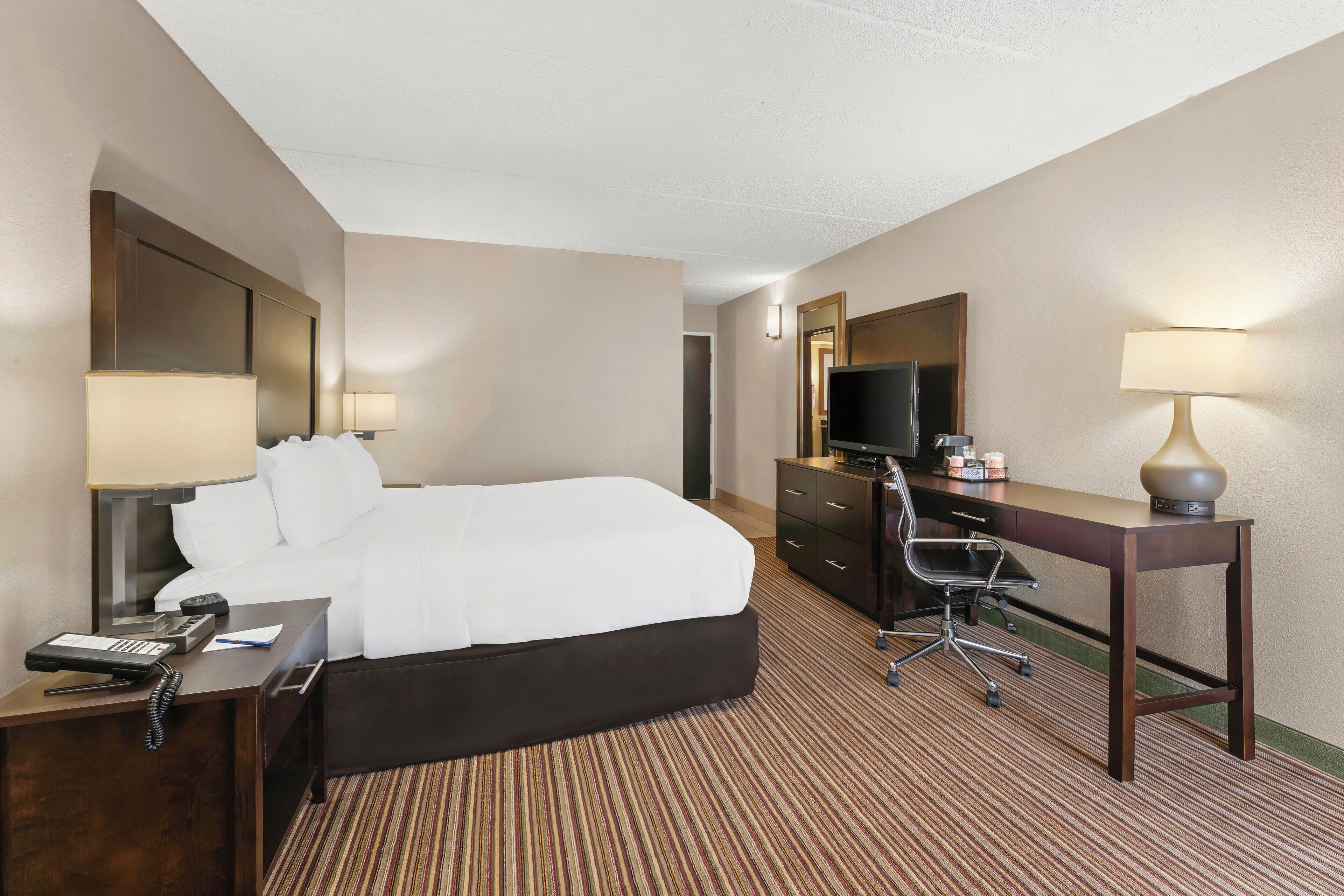 Une chambre d’hôtel avec un grand lit, un bureau avec un ordinateur, une télévision et une lampe.