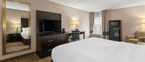 A hotel room with a large bed, a TV, a desk with a lamp, a microwave, and a sofa.