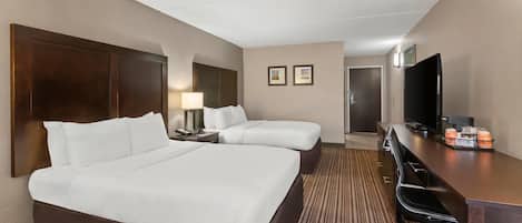 A hotel room with a large bed, a smaller bed, a desk with a chair, a television, and a door leading to another room.