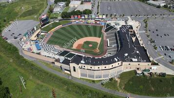 Vista aérea de un estadio de béisbol con un amplio estacionamiento, un marcador y un campo central.