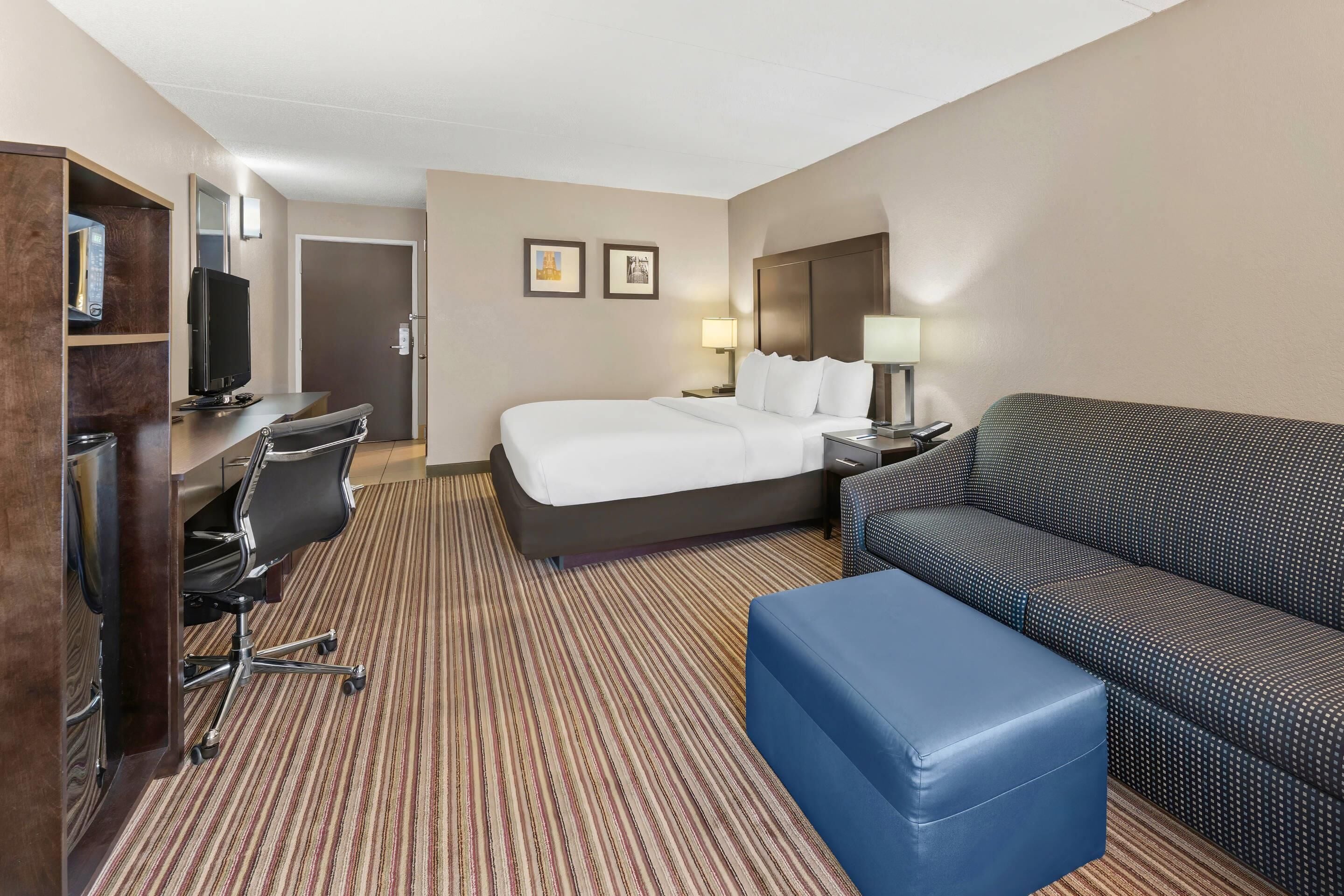 A hotel room with a bed, a desk with a computer, a sofa, and a TV.