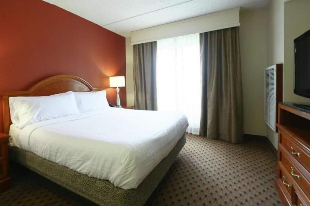 A hotel room with a bed, two bedside tables, a TV, and a window with curtains.