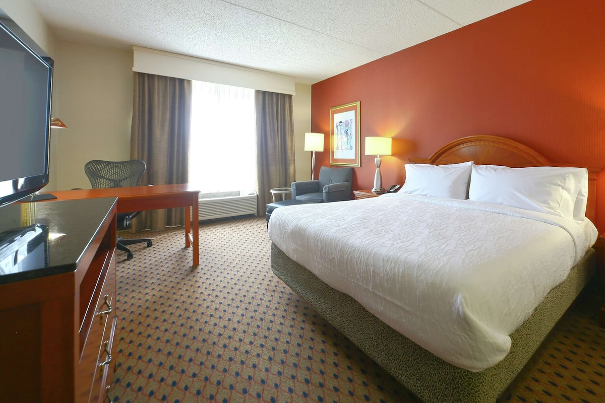 A hotel room with a large bed, a desk, a chair, a television, and a lamp.