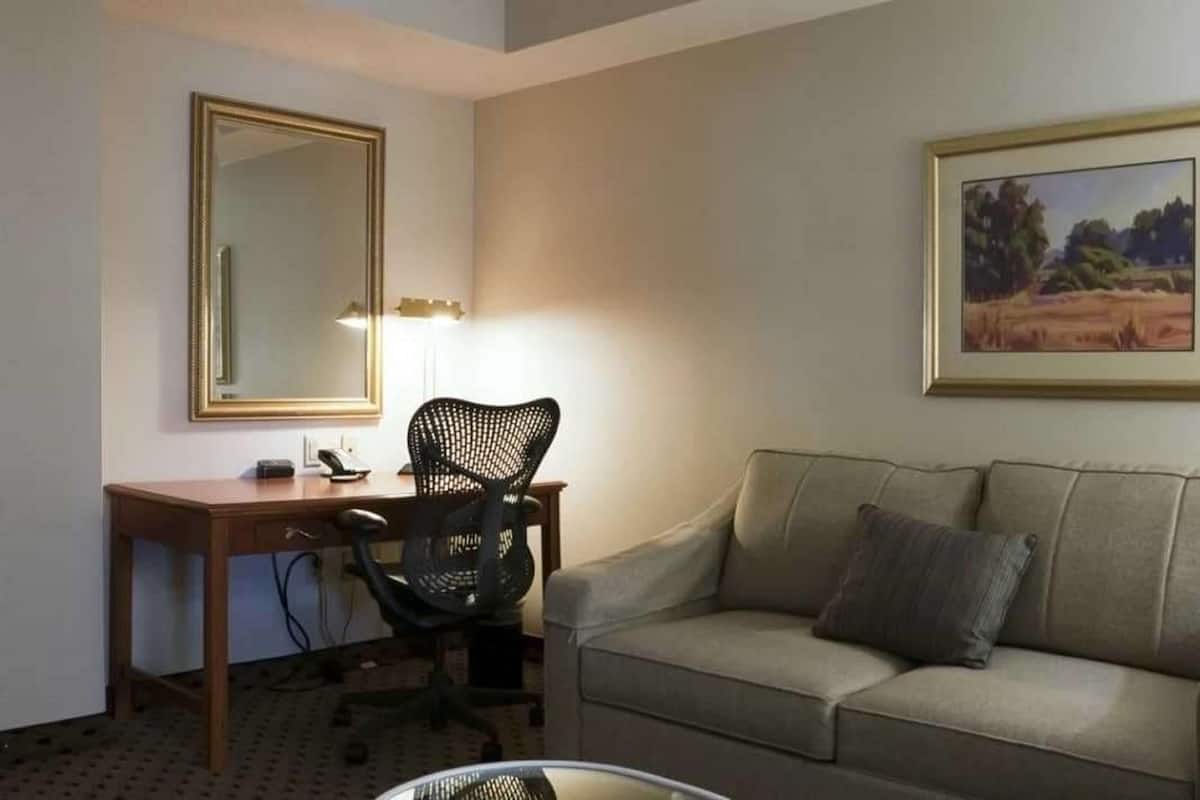 A room with a desk, chair, and sofa. There is a mirror on the wall and a painting above the sofa.