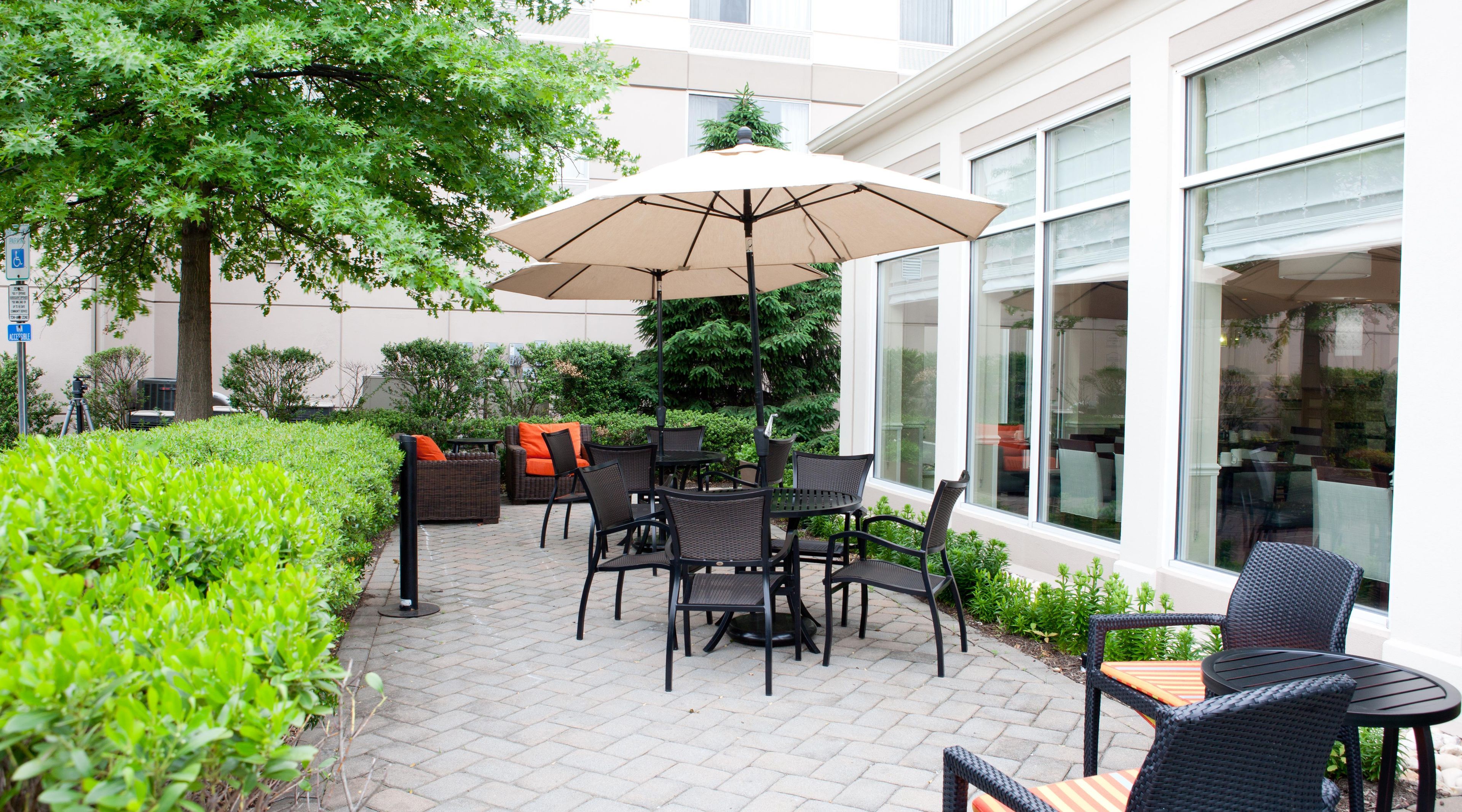 An outdoor patio with a table and chairs, surrounded by greenery and a large umbrella.