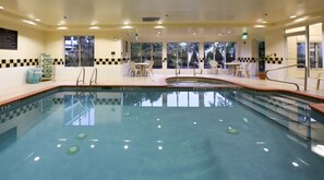 Una piscina interior con agua cristalina, zona poco profunda y unas escaleras de acceso. Hay sillas y mesas alrededor de la piscina, y un cartel que indica la profundidad del agua.
