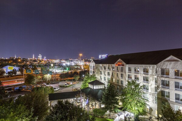 Un hotel de varios pisos, un jardín en la azotea y vista panorámica de la ciudad de noche.