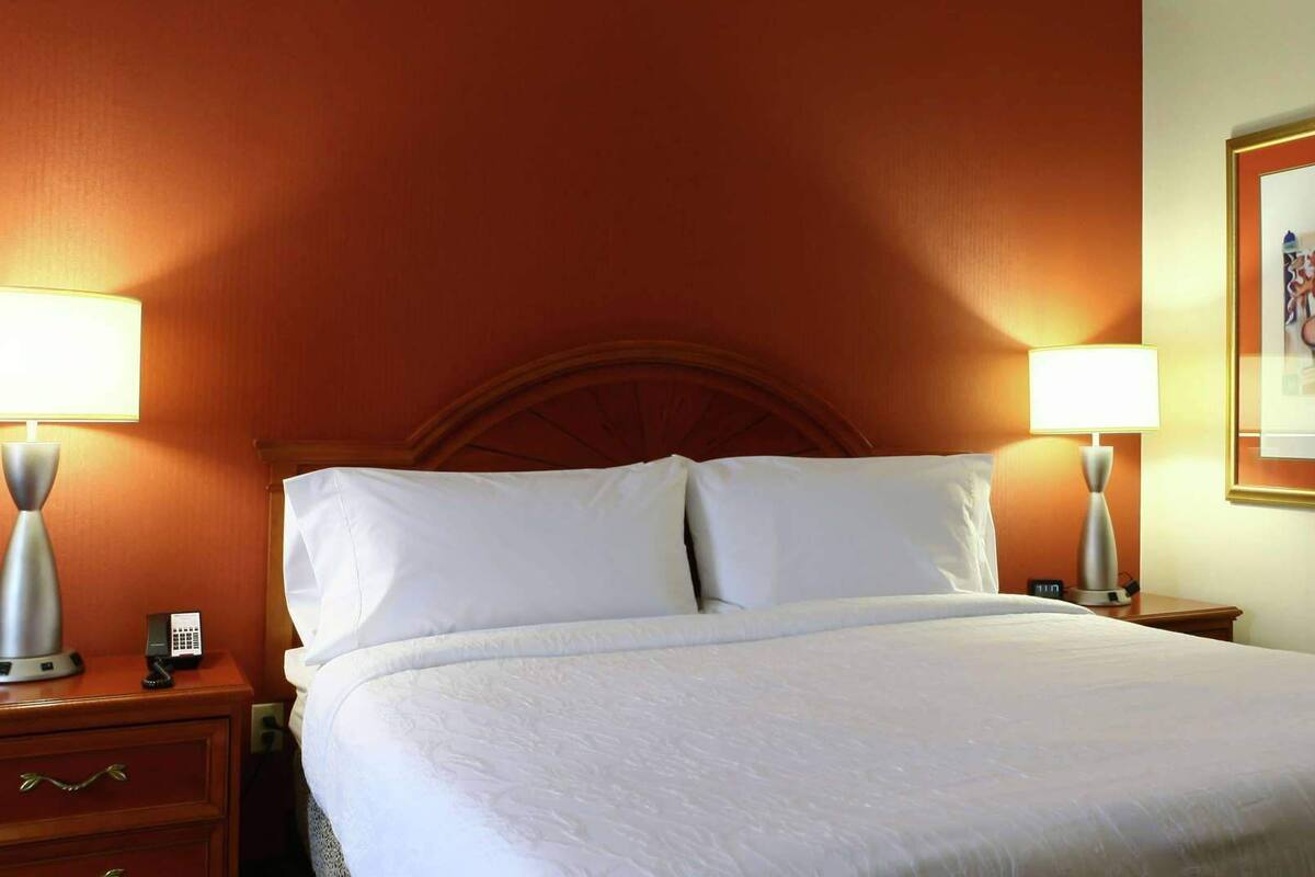 A hotel room with a bed, two bedside lamps, a nightstand, a telephone, and a framed picture on the wall.