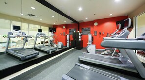 Une salle de sport équipée de tapis de course, d’un vélo d’appartement et d’un mur recouvert de miroirs.