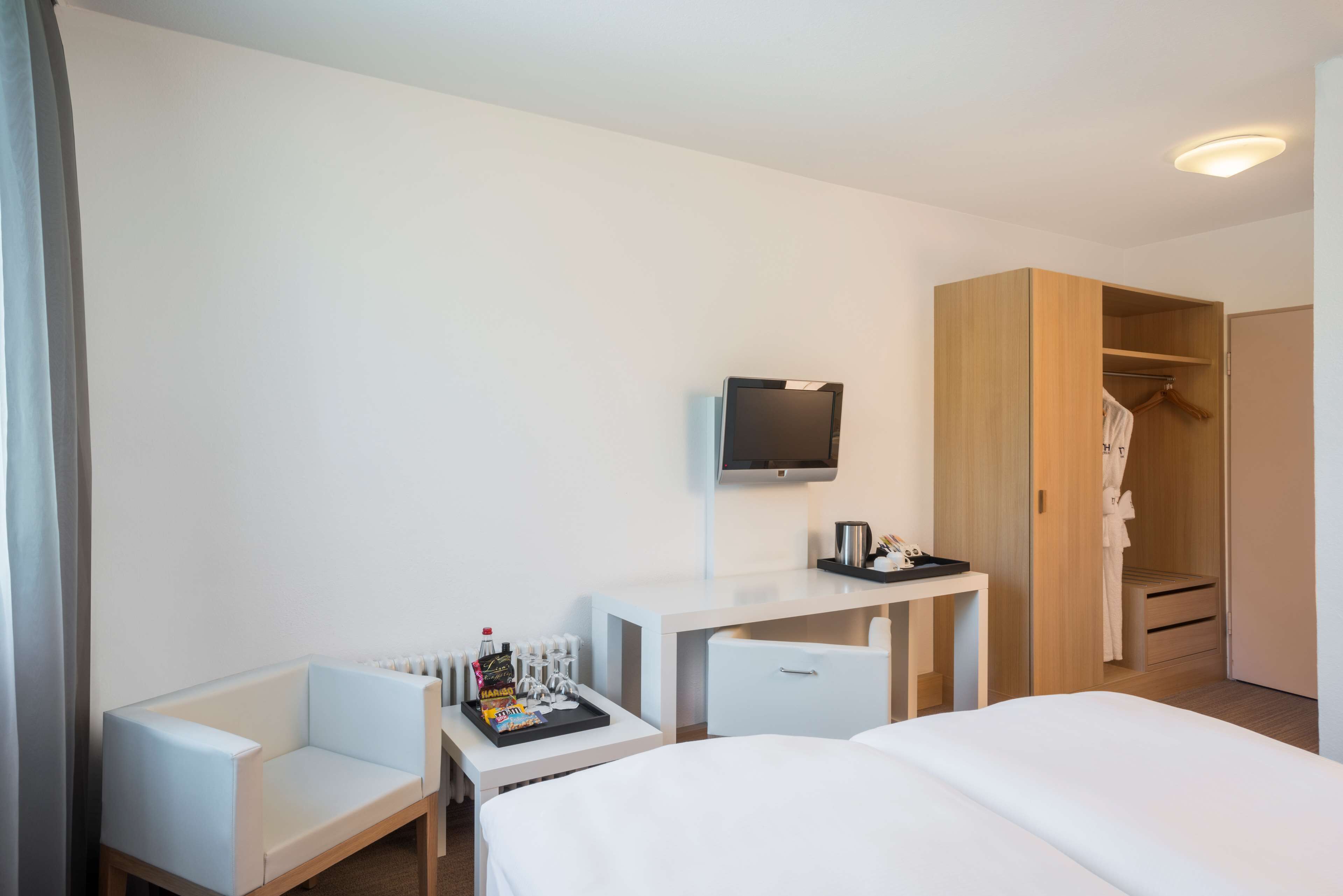A hotel room with a bed, a desk with a flat-screen TV, a seating area, and a walk-in closet.