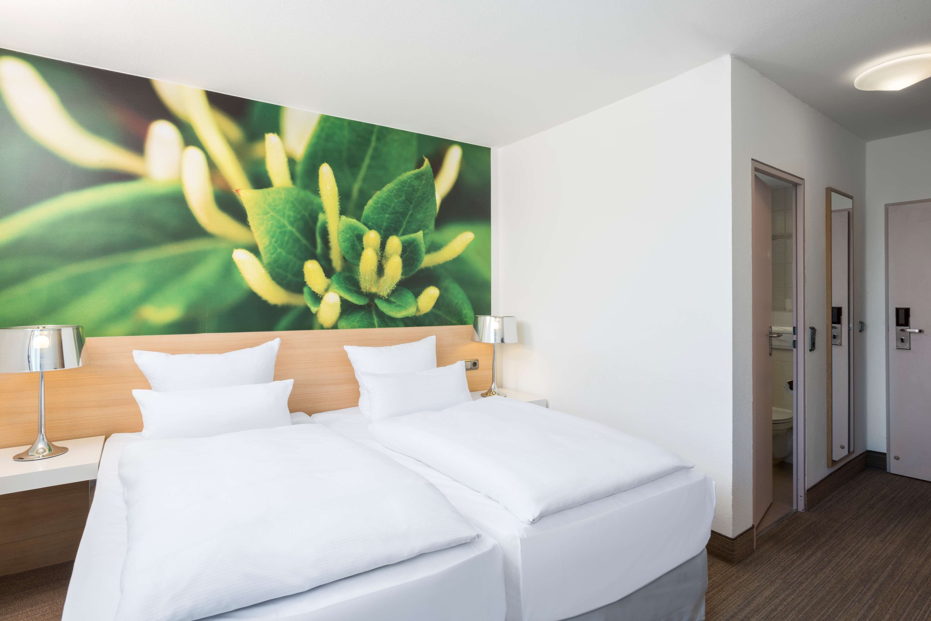 A hotel room with a bed, a nightstand, a lamp, and a large floral artwork on the wall.