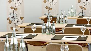Ein Konferenzraum mit für Meetings gedeckten Tischen, ausgestattet mit Wasserflaschen und Gläsern, und mit floralem Wandpapier dekoriert.