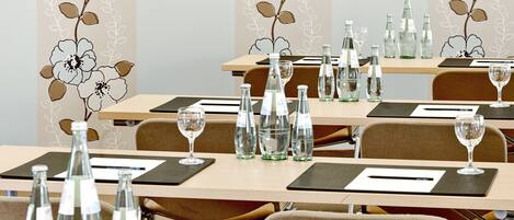 Ein Konferenzraum mit für Meetings gedeckten Tischen, ausgestattet mit Wasserflaschen und Gläsern, und mit floralem Wandpapier dekoriert.
