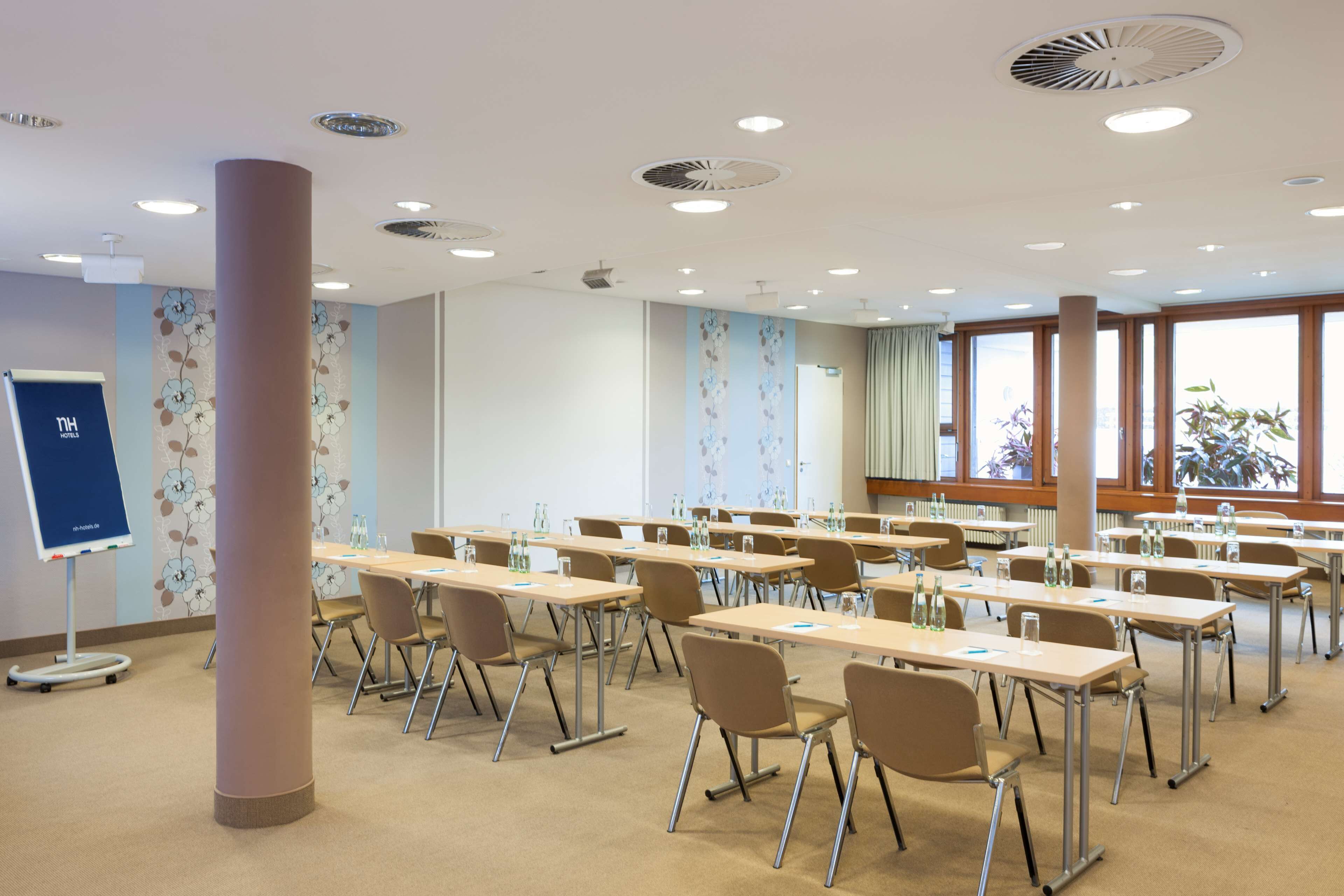 A conference room with multiple tables and chairs, a whiteboard, and large windows with a view of trees.